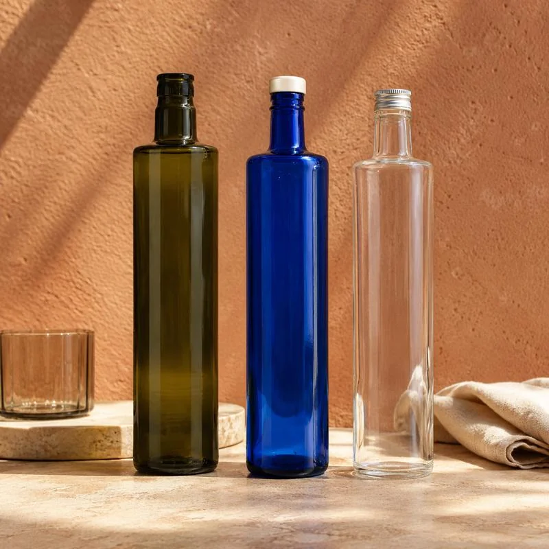 Tre bottiglie slanciate nei colori verde, blu e trasparente su fondo terracotta